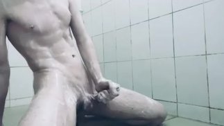 Een jonge man met een grote lul scheert en masturbeert in een openbare douche
